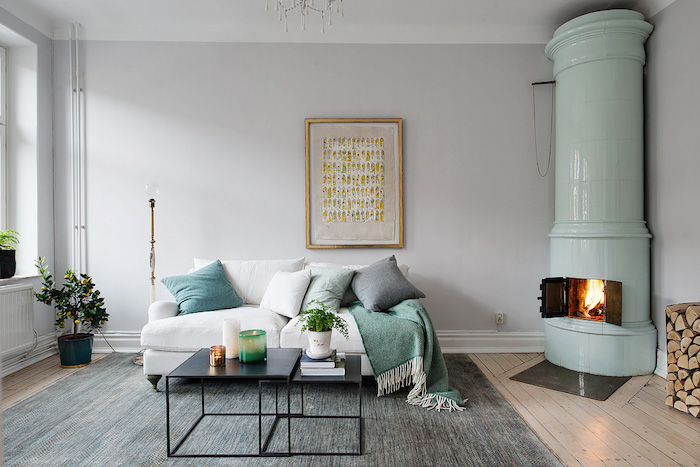 style scandinave, canapé blanc avec coussins décoratifs, cheminée verte de coin, parquet en bois, table basse en noir