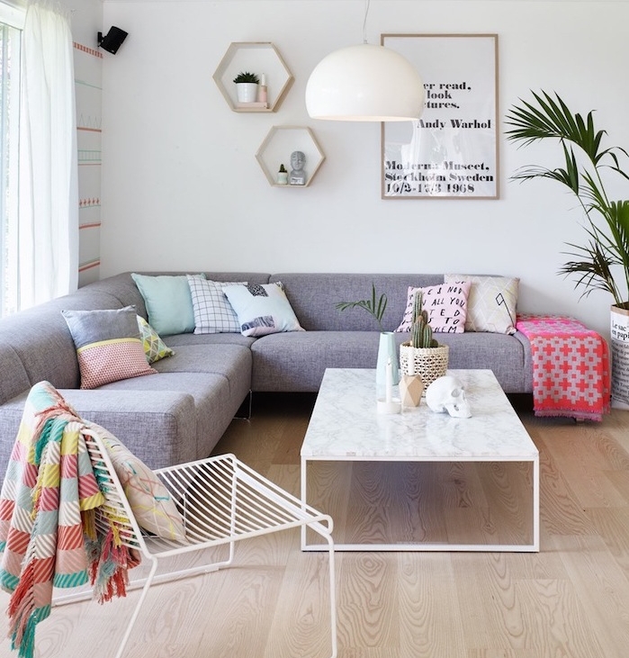 salon scandinave, canapé d'angle en tissu gris, plaid en rouge et rose, table basse en marbre, rideaux longs en blanc