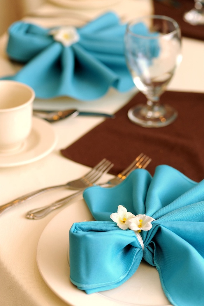 technique origami pour faire une déco de table élégante, pliage de serviette en tissu bleu avec rond florale