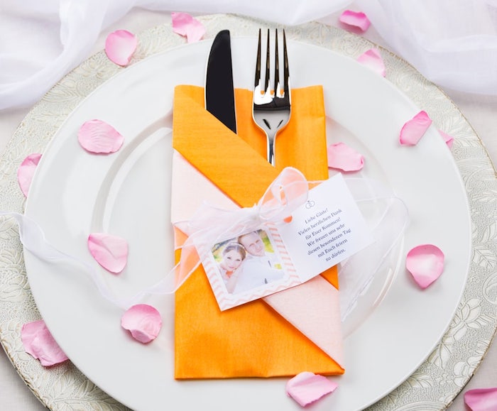arrangement de table mariage, serviette origami en orange avec photo couple et ruban, feuilles de rose