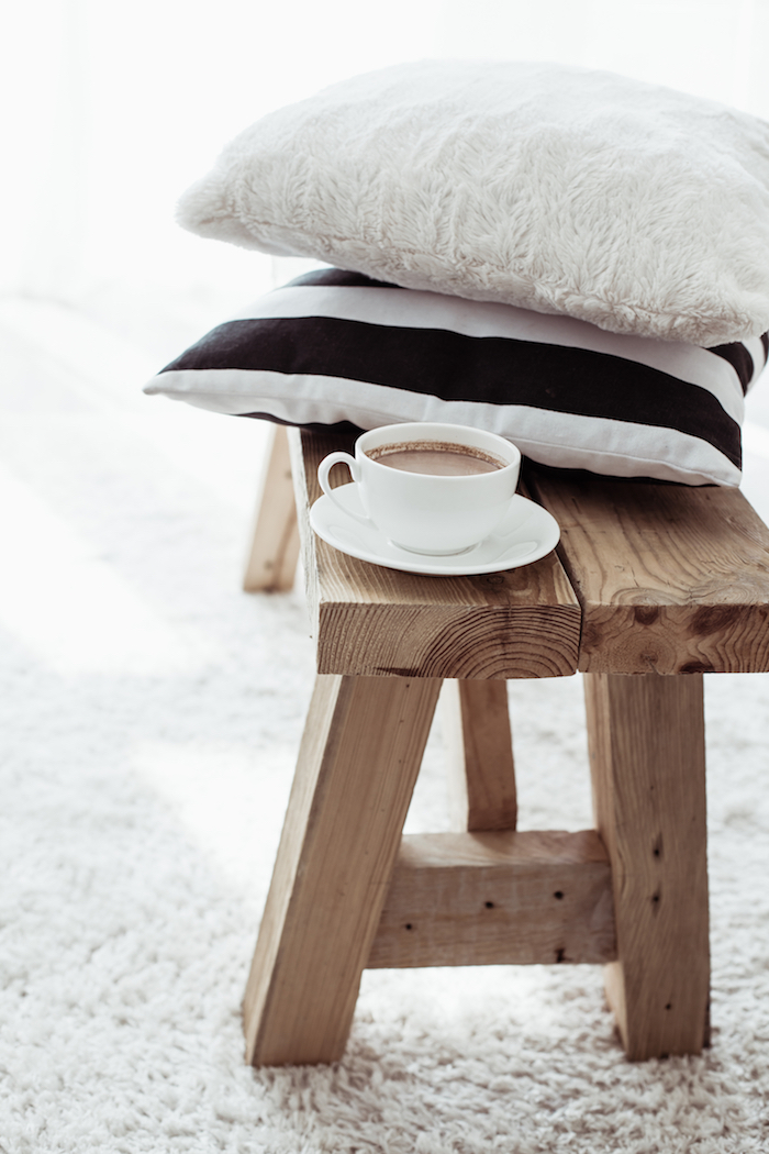intérieur scandinave, table basse en bois, tasse de café, coussins décoratifs en blanc et noir, tapis moelleux en blanc