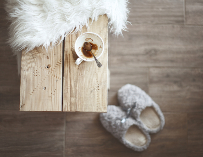 ambiance scandinave, parquet en bois, chaussons gris avec ruban, petite table à café, housse en faux fur blanche