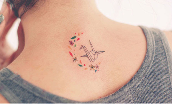un petit tatouage minimaliste à la nuque mêlant des motifs floraux et une grue en origami