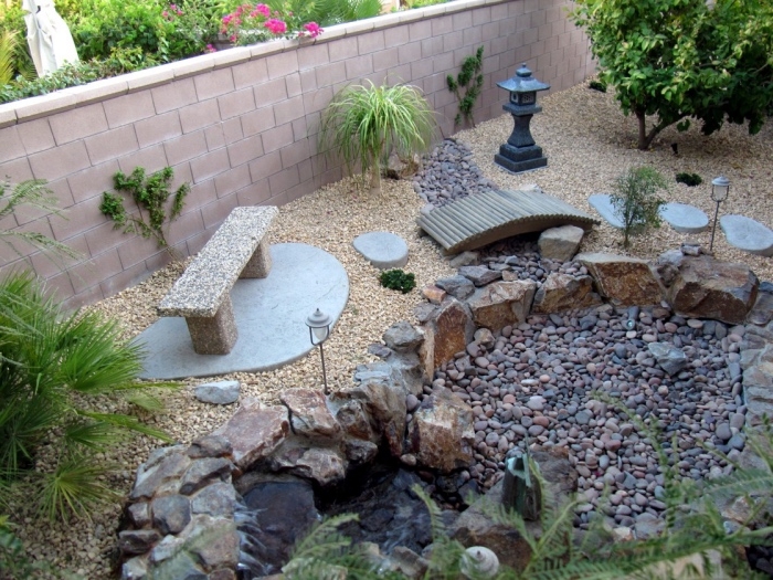 decoration zen jardin, une chute d eau, entourée de grosses pierres, avec une bassin de galets et gravier pour le reste, un petit pont en bois et banc en pierre pour se détendre, lanterne