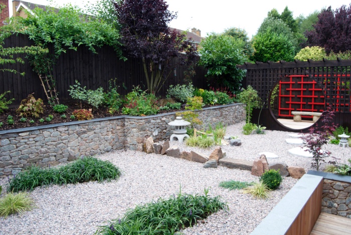 jardin zen japonais, un bassin recouvert de gravier, petits arbustes verts, lanterne en pierre, plus grosses pierres, cloture en bois