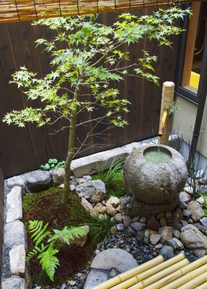 fontaine d eau dans un carré zen du jardin, decoration zen de galets, pierres, bambou et arbre, cloture en bois et bambou