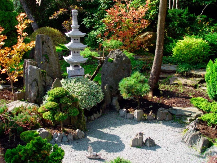 jardin zen minimaliste, gravier, pierres sur le sol, arbustes et petits arbres, petit temple en pierre, vegetation verte