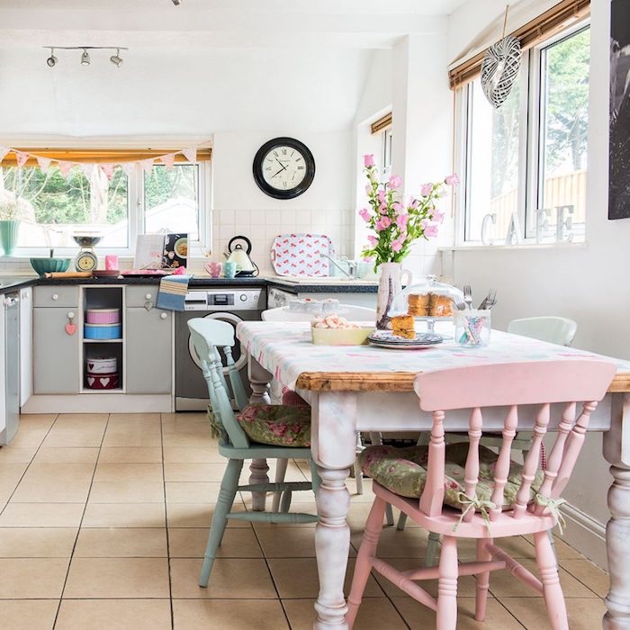 façade cuisine, table en bois et marbre, carreaux beige, mur couleur blanche, chaises en bois bleu et rose pastel, horloge vintage