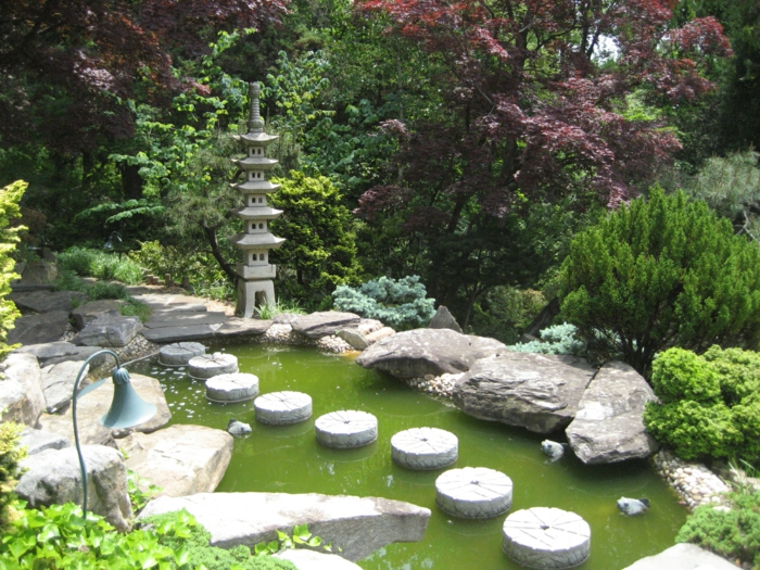 idée amengament jardin zen japonais, un chemin de pierres dans un bassin d eau, statuette temple japonais, arbres et arbustes