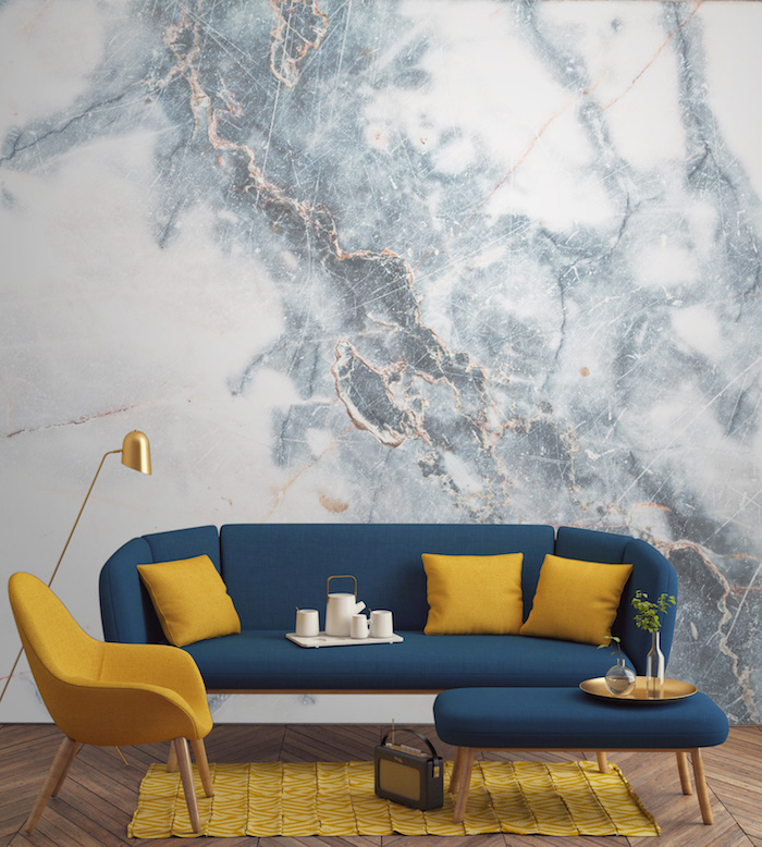 marbre blanc, aménagement de salon, revêtement de sol en bois, canapé en bleu foncé avec coussins jaunes, lampe sur pied en cuivre