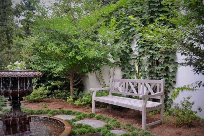idee deco jardin simple, fontaine, banc en bois, chemin de pierres, plantes grimpantes sur un mur, arbres et arbustes