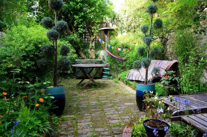 comment paysager son jardin, un espace détente en dalles de pierre, un banc et une table de jardin, petits arbres et arbustes autour