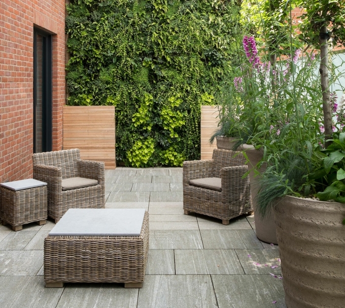 idée de génie jardin, patio salon de jardin en dalles de pierre, fauteuils et tables en rotin, mur végétal et gros pots de fleurs 