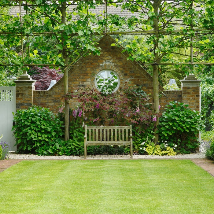 amenagement jardin exterieur, un gazon vert avec une bordure d arbustes et des fleurs, arbres, clôture en briques, cadre nature campagne