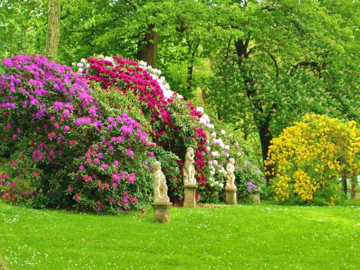 idee amengament jardin paysager, gazon bordé d arbustes fleuris, statuettes en pierre, arbres, cadre naturel campagne