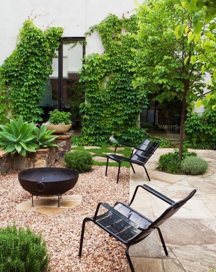 aménager son jardin, un espace barbecue avec des chaises noires en metal, mur envahi de lierre, plante grimpante, maison de campagne, dalles de pierre