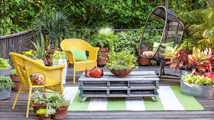 aménager son jardin sur une terrasse, une table en palette à roulettes, chaises tressées jaunes, revêtement en teck, balançoire suspendue en bois, plusieurs plantes dans des pots de fleurs