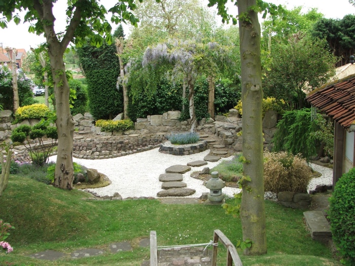 modele amenagement jardin zen, pelouse avec des arbres, chemin de pierres, lanterne, gravier blanc, arbres et buis, vegetation verte en profusion