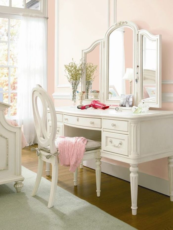 coiffeuse blanche, chaise et miroir, lit blanc baroque, tapis gris, mur couleur rose pastel, rideaux blancs, grandes fenêtres
