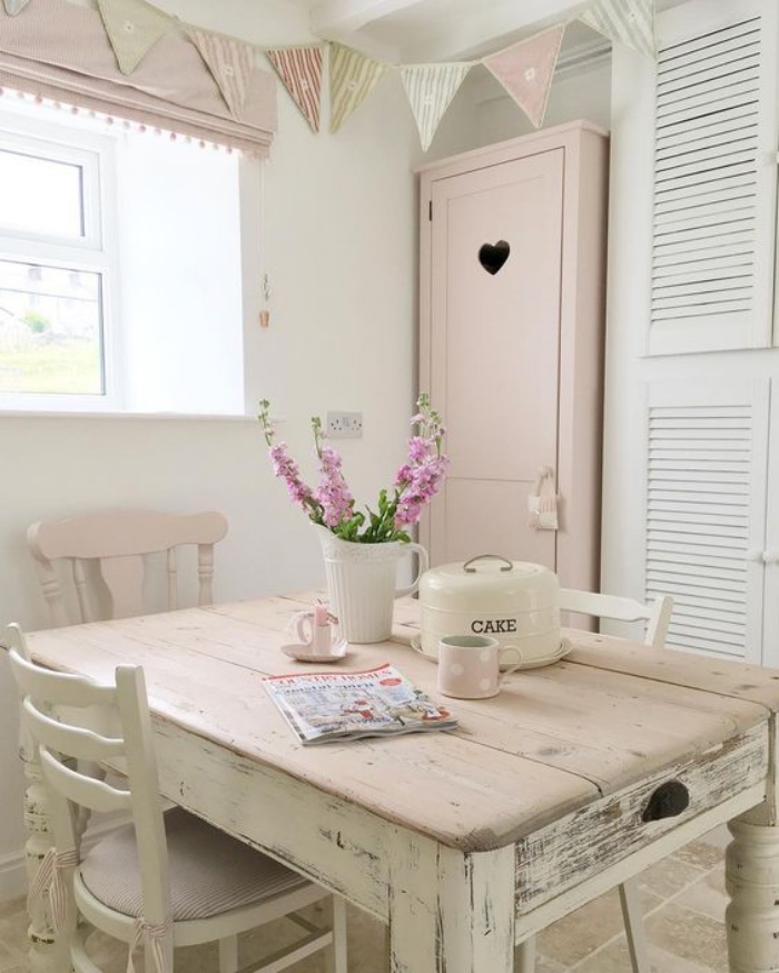 shabby chic decoration dans la cuisine, table en bois massif patiné, chaises en bois, armoire rose, meuble de rangement blanc, carreaux en pierre, guirlande de fanions