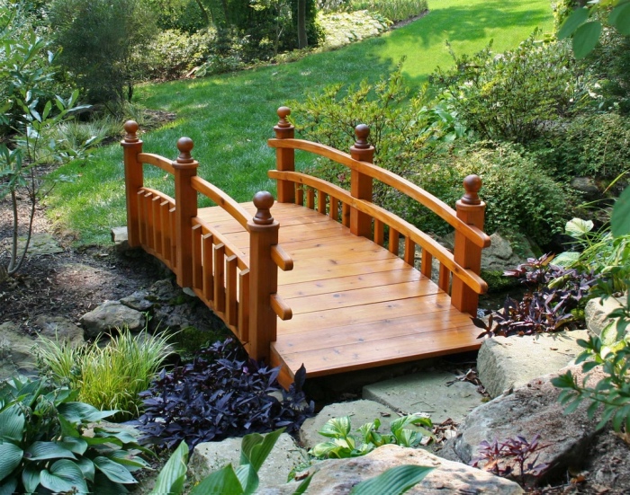 element essentiel du jardin zen, petit pont en bois, arbustes, pelouse et pierres, vegetation verte