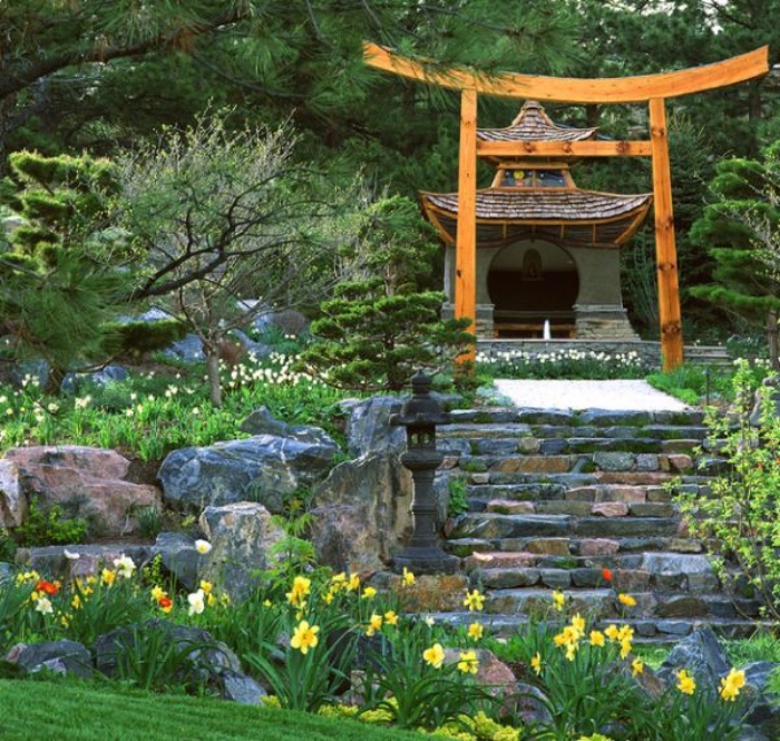 idée de jardin zen adjacent à un temple japonais, escalier en pierre, entouré de grosses pierres, pelouse et fleurs fraiches