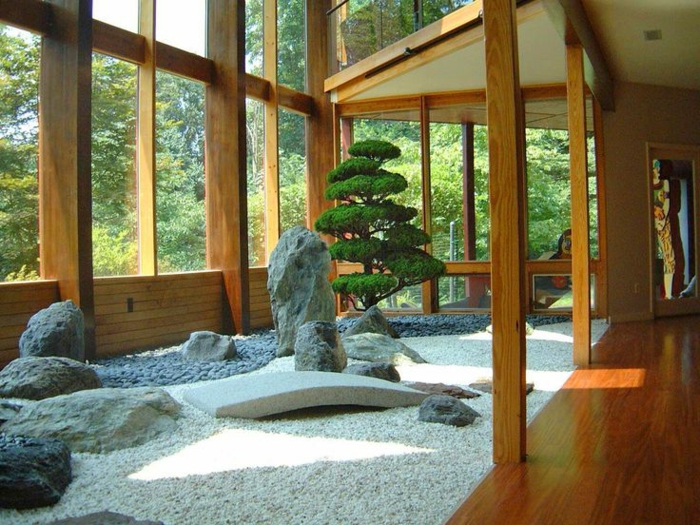 jardin zen a l interieur d une maison charpente en bois, gravier, galets et pierres, imitant des montagnes, arbre japonais, grosses fenêtres