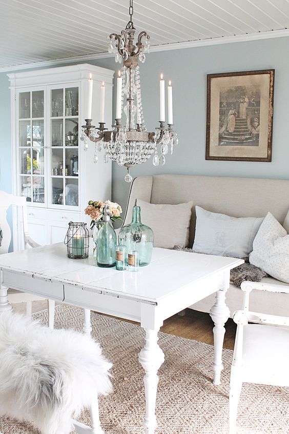 salon shabby chic decoration, table et chaises blanches, mur couleur bleu pastel, lustre élégant, decoration de table bouteilles en verre, vaisselier blanc