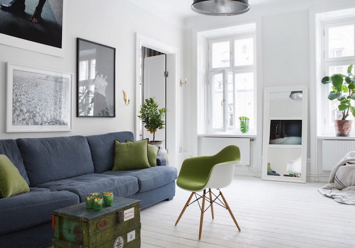 salon scandinave, parquet en bois peint en blanc, suspension luminaire métallique, canapé en tissu bleu foncé, coussin en vert