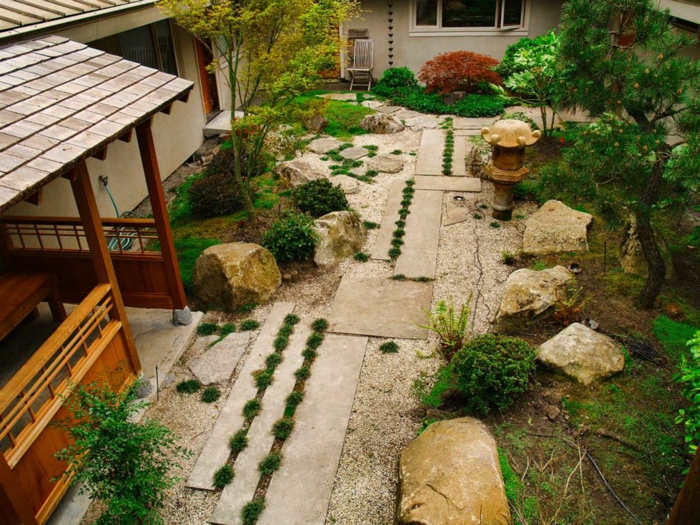 decoration zen dans le jardin, sol en gravier, chemin entouré de pierres, arbres et arbustes verts