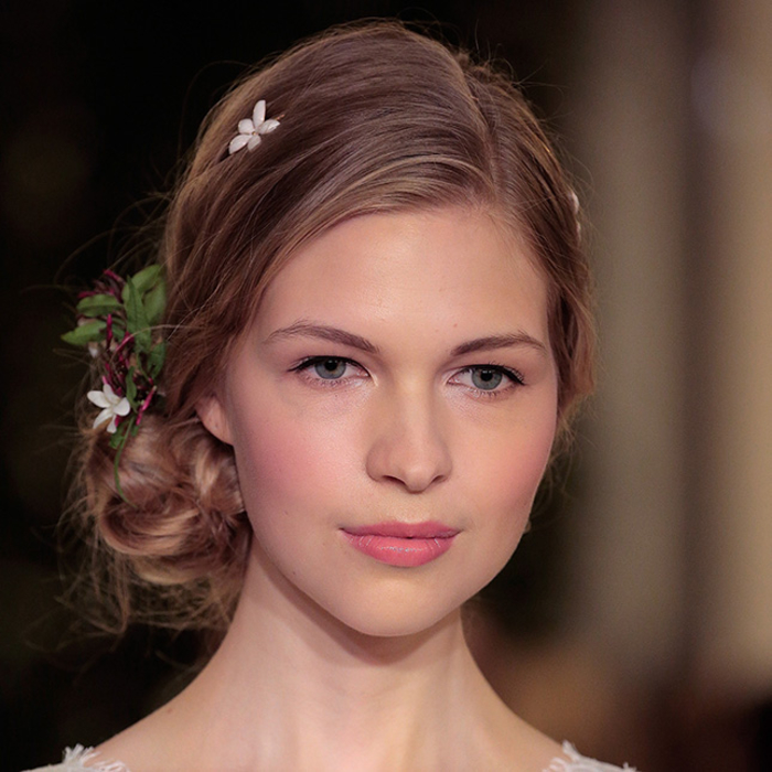 une vision de mariée romantique réalisée avec un maquillage discret aux nuances de rose complétée par un chignon bas décoré de fleurs