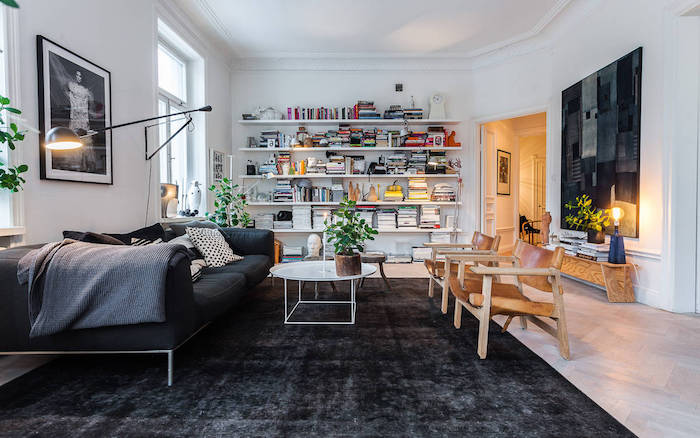 deco esprit scandinave, bibliothèque à livres et objets décoratifs, canapé noir avec coussins, table basse en blanc, chaises en bois