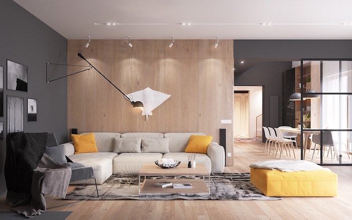 meuble scandinave, mur peint en gris foncé, revêtement de mur en bois, canapé d'angle beige, tabouret en jaune moutarde
