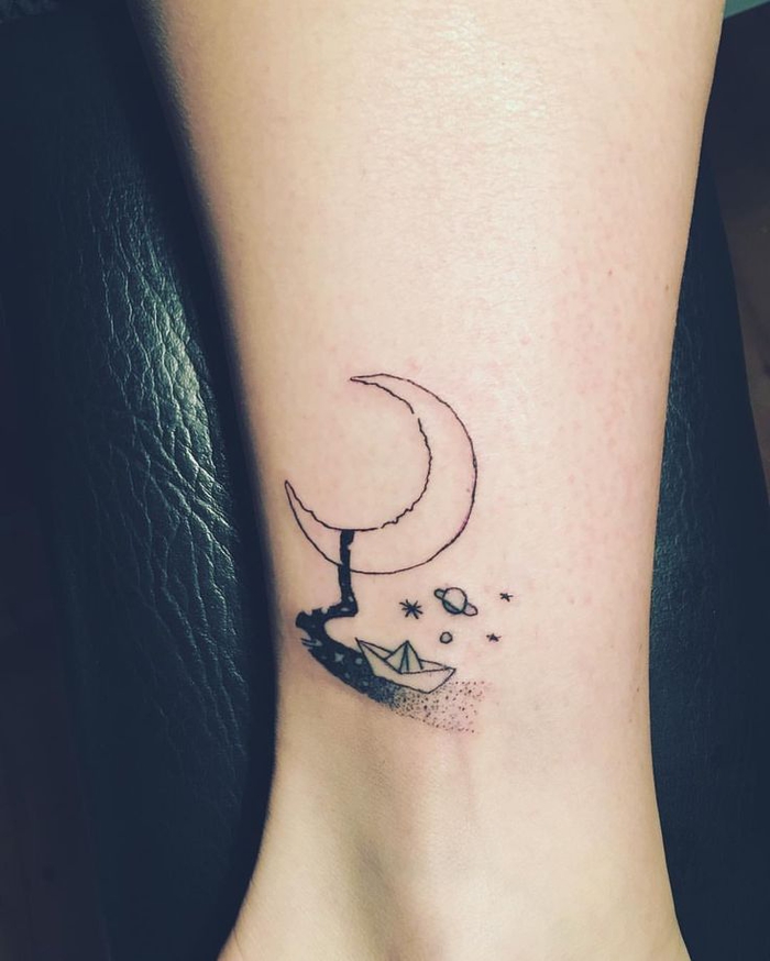 un tatouage minimaliste ciel et mer avec un petit bateau en origami et un croissant de lune graphique