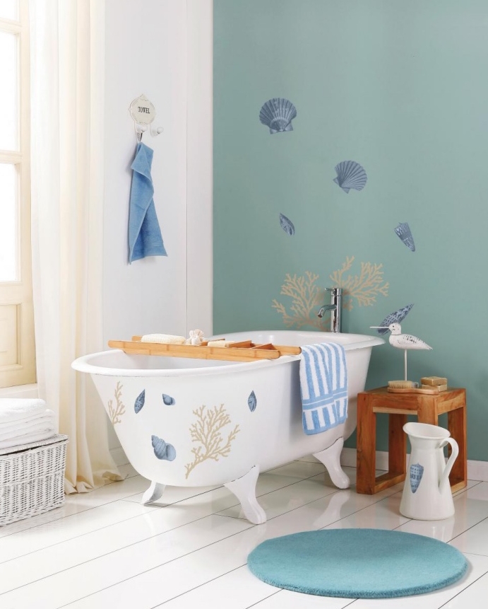 mur d accent vert pastel, thème bord de mer, parquet blanchi, baignoire à poser, tapis rond, rideaux blanches et panier de rangement serviettes