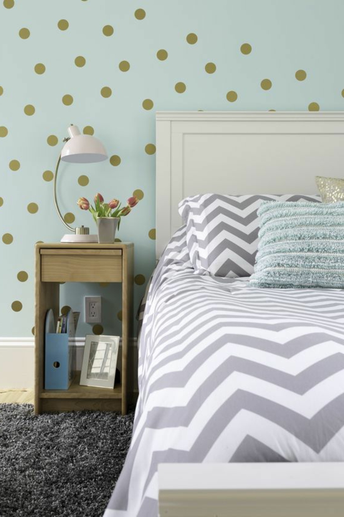 chambre, mur peinture vert d eau à pois dorés, tapis gris anthracite, linge de lit blanc et gris, table de nuit en bois 
