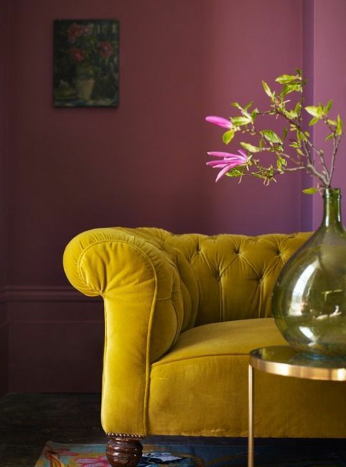 peinture aubergine, table basse ronde, sofa moutarde capitonné, vase avec des fleurs, 