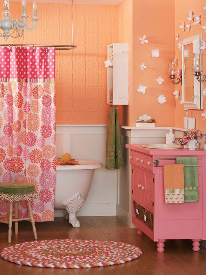 petite salle de bain aux murs couleur peche et rose et rideaux en fleurs et pois un lustre baroque au plafond 