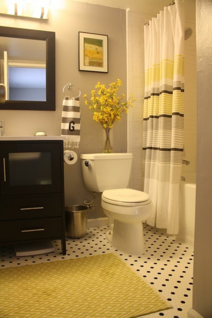 petite salle de bains avec rideaux blancs aux rayures jaunes et marron avec tapis jaune meubles noirs