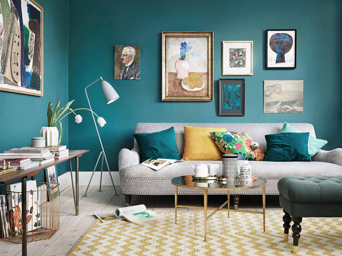 un salon cozy qui associe le bleu paon aux tons ocre, mur en cadres qui reprennent les mêmes nuances