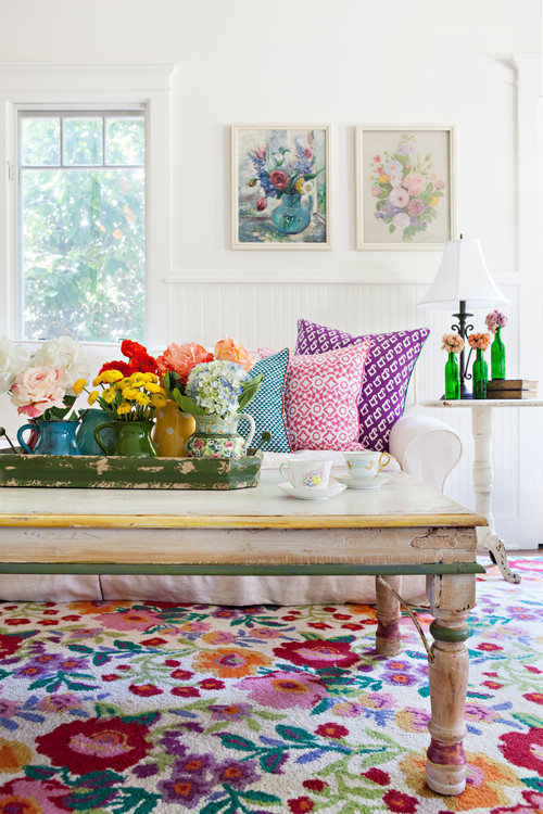 canapé shabby chic blanc, tapis et coussins multicolores motifs imprimés floraux, table en bois brut, decoration de fleurs, mur couleur blanche, peintures de fleurs