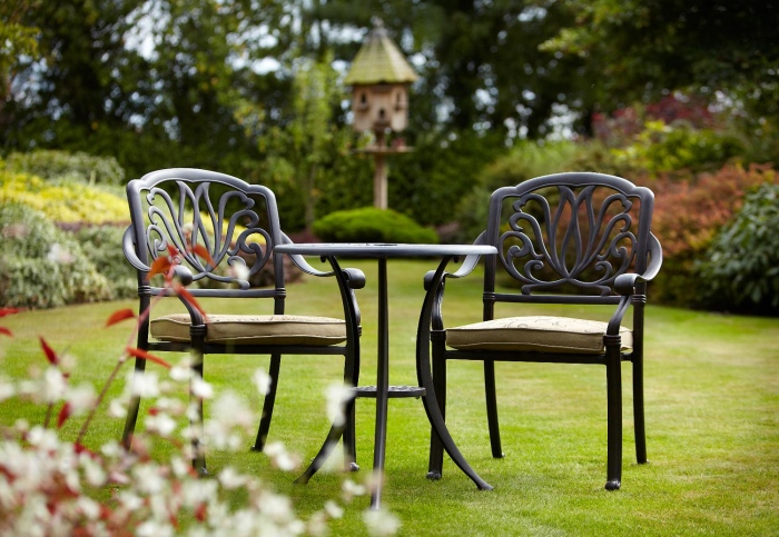 salon de jardin simple sur un gazon, table ronde noire er chaises noires avec des coussins d assise beige, plusieurs arbustes et arbres en bordure