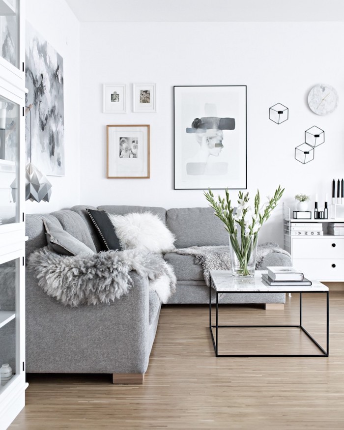 appartement scandinave, murs peints en blanc, canapé d'angle en gris, table en marbre et fer forgé, vase en verre avec fleurs blanches