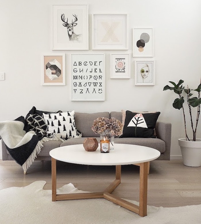 meuble scandinave, canapé beige avec coussins décoratifs, table basse ronde avec pieds en bois, cadres photos avec art prints