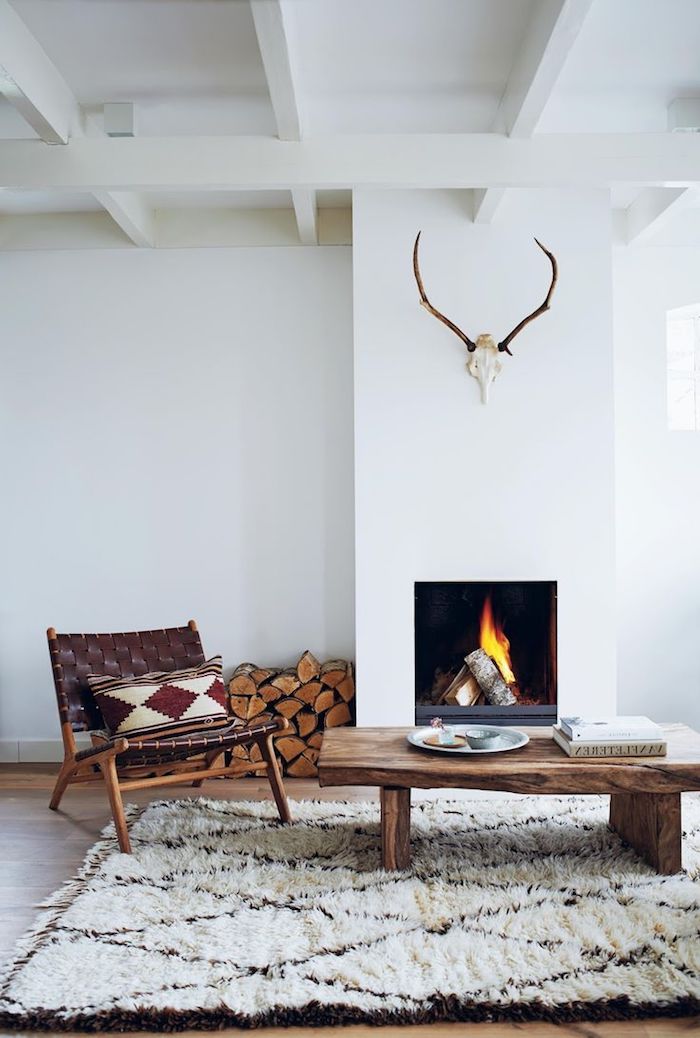 deco scandinave, cheminée blanche, cornes de cerf en bois, chaise en bois marron, table basse en bois, tapis blanc et marron