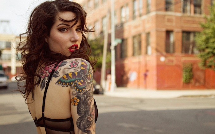 femme tatoué, coiffure avec boucles en marron foncé, maquillage avec rouge à lèvre, tatouage sur le bras