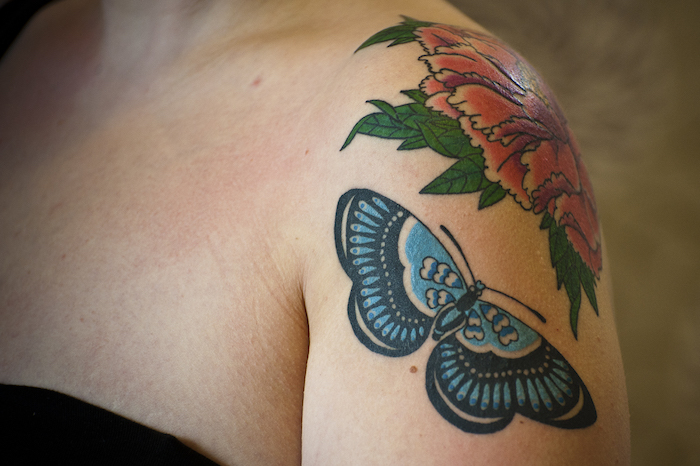 tatouage papillon, dessin en couleurs sur l'épaule, tatouage avec fleur rouge et papillon bleu