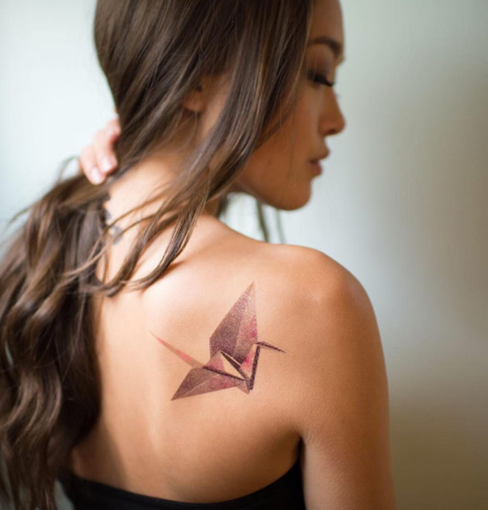 un tatouage géométrique rose et mauve en forme de grue inspiré par l'art de l'origami