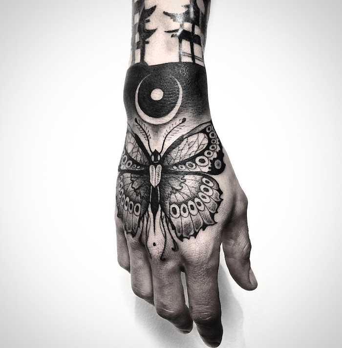tatouage papillon, silhouette papillon avec motifs tribals sur la main, idée design tattoo total noir