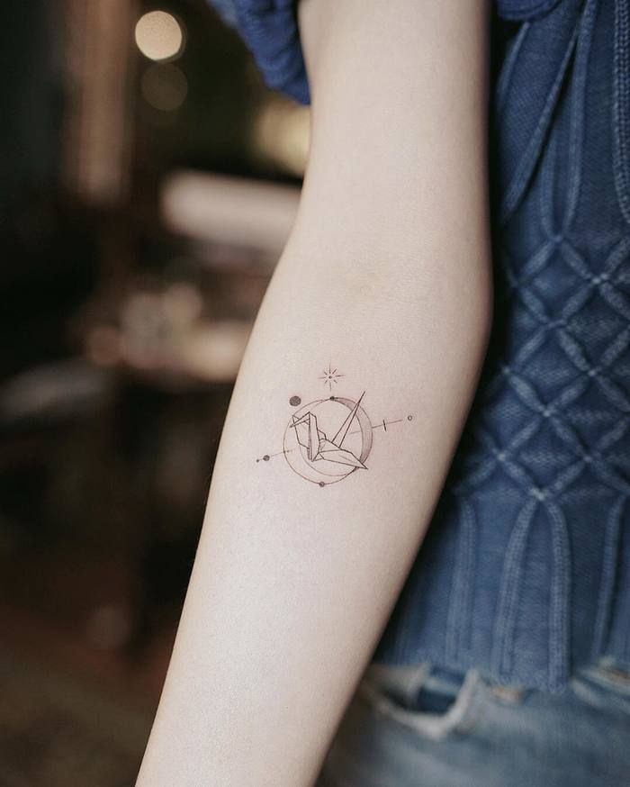 un tatouage minimaliste représentant une grue origami placée au centre d'une sphère armilaire